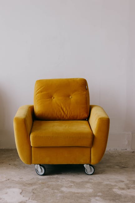 Close-up of a patterned fabric sofa with a decorative floral cushion in shades of yellow, red, and green, and a plain beige cushion with a stitched border, all set on a plush, beige upholstered surfac